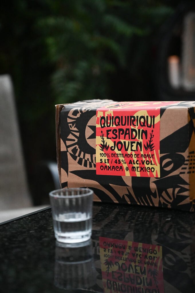 A box of mezcal sits next to a veladora